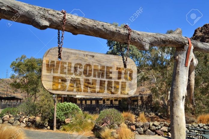 old vintage wood signboard with text " welcome to Banjul" hanging on a branch