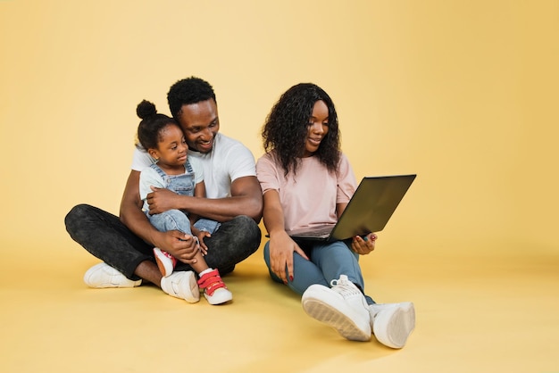 jeunes-parents-africains-assis-sol-leur-fille-embrassant-aide-ordinateur-portable-pour-appel-video_161094-10981